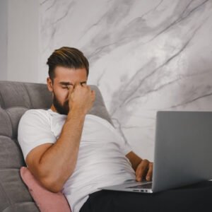 A man sitting on his couch late on Sunday evening, looking stressed while staring at his laptop, dreading Monday morning.
