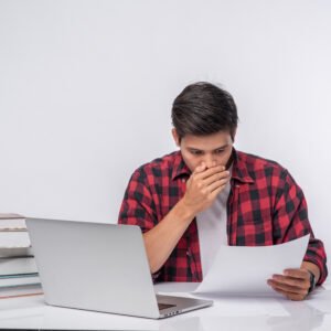 A man sitting at his desk holding a document, squinting in concentration as he struggles to read the text.