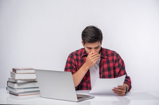 A man sitting at his desk holding a document, squinting in concentration as he struggles to read the text.