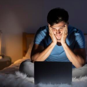 A man sitting on his couch on Sunday evening, staring at his laptop with a worried expression as he thinks about the work week ahead.